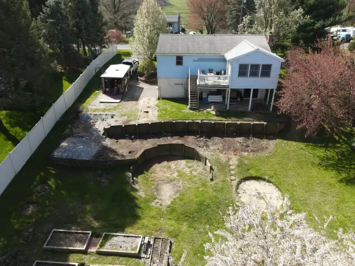 Aerial view of a residential backyard with an existing timber retaining wall, lawn, garden beds, and the rear of the home.