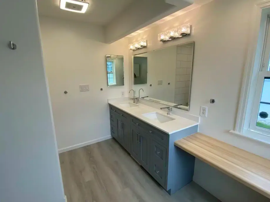 Remodeled master bathroom with a blue double vanity and a built-in wood bench